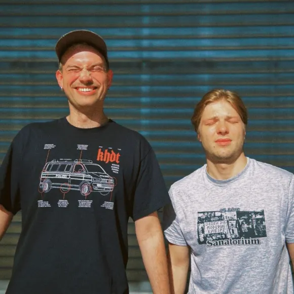 Regieassitent Georg Dirlack grinst, Schauspieler Fabian Reichenbach verzieht das Gesicht.