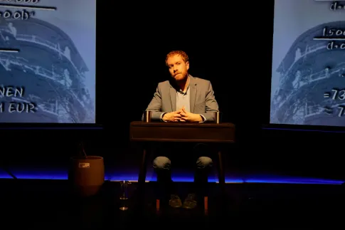 Calle Fuhr sitz an einem Tisch im Bühnen Bild von Aufstieg und Fall des Herrn René Benko