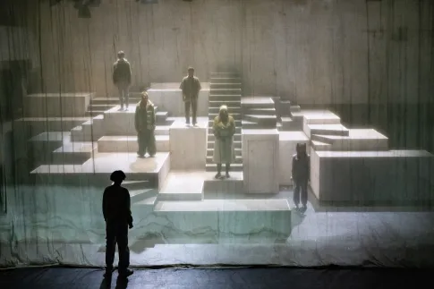 Ein Kind steht vor einem Vorhang. Dahinter sieht man schemenhaft ein Labyrinth mit weiteren Kindern