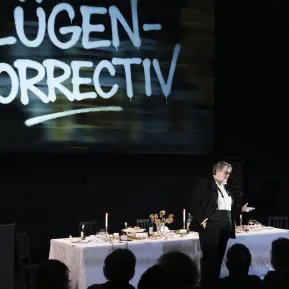 Andreas Beck steht vor einer gedeckten Tafel, hinter ihm ist "Lügen Correctiv" auf einer Leinwand projiziert