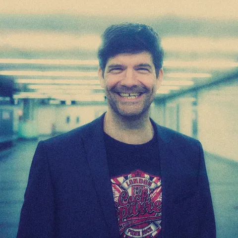 Frank Genser steht in diffusem Licht in einer U-Bahn Station und grinst in die Kamera
