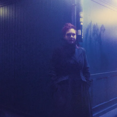Anke Zillich lehnt an einer Regenrinne am Wiener Naschmarkt, Bild in blauem Licht